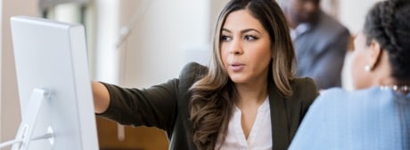 A woman points at a computer screen while explaining something to a client.