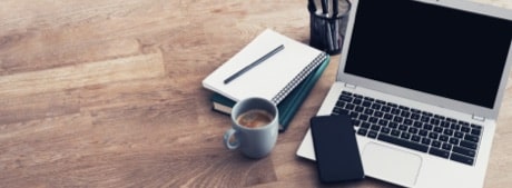 A laptop computer sitting on a desk next to a coffee, notepad, and phone.